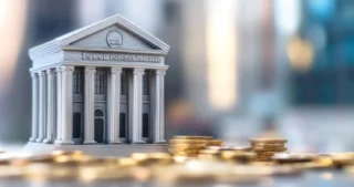 Maqueta de un edificio bancario clásico con columnas, rodeada de monedas apiladas, que simboliza la transferencia bancaria y los métodos de pago financieros.